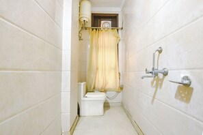 A small, narrow bathroom with white tiled walls, a toilet, a shower with a curtain, and a wall-mounted faucet.