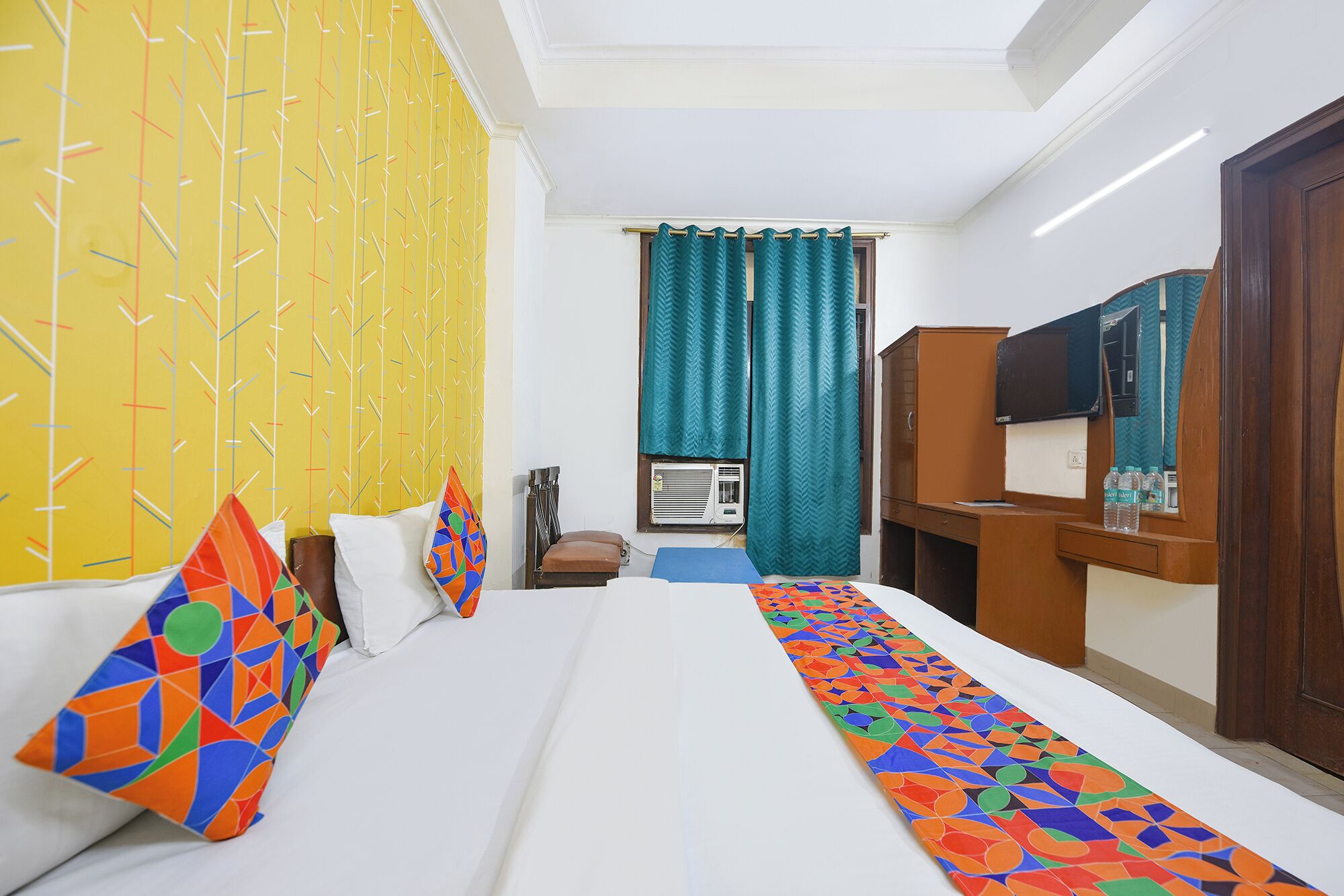 A hotel room with a large bed, a desk, a television, and a window with curtains.