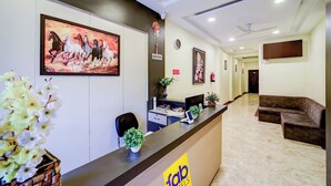 A hotel reception area with a reception desk, a clock, a reception sign, and a couch. - Fabhotel The Shloka (Bhopal)
