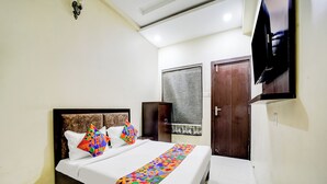 A neatly made bed with colorful pillows and a patterned bedspread, a wooden wardrobe, a television mounted on the wall, and a window with curtains. - Fabhotel The Shloka (Bhopal)