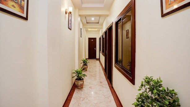 A hallway with a marble floor, potted plants, framed artwork, and wooden doors. - Fabhotel The Shloka (Bhopal)