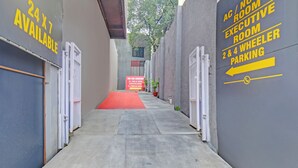 A hallway with a red carpet leading to a building entrance. There are signs indicating "AC / NON ROOM EXECUTIVE ROOM 2 & 4 WHEELER PARKING" and "24 X 7 AVAILABLE". - Fabhotel Sri Sai (Pune)