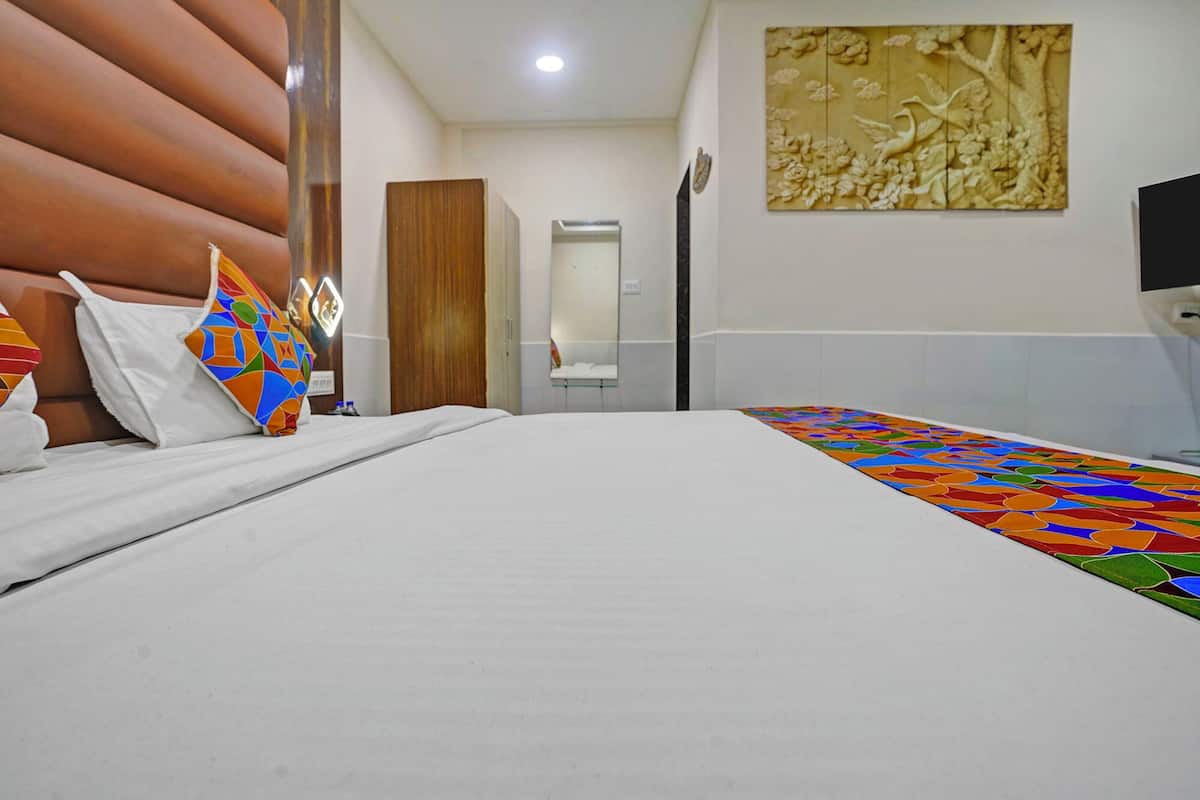 A hotel room with a large bed, a wooden headboard, a colorful throw, a mirror, and a wall-mounted artwork.