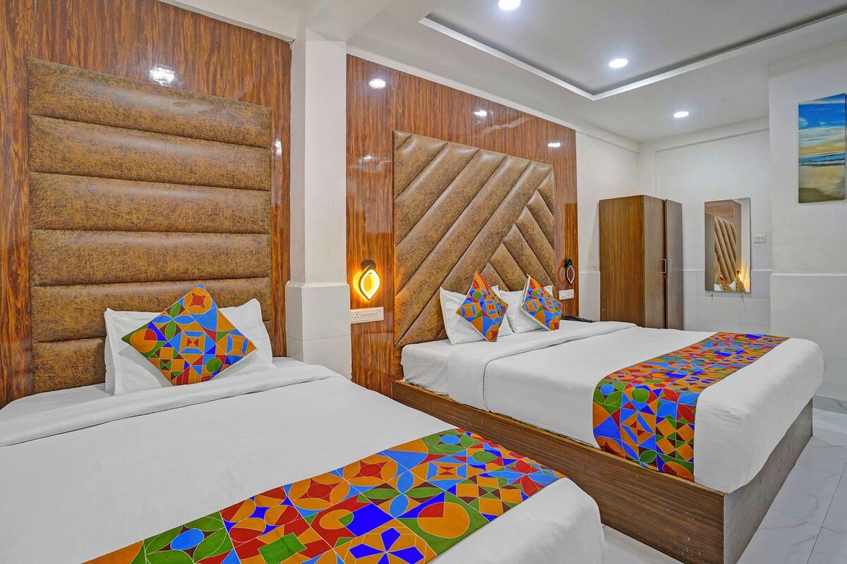 A hotel room with two beds, wooden headboards, a modern light fixture, and a painting on the wall.