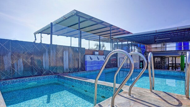 A swimming pool with clear blue water, a covered seating area, and a view of the surrounding area. - Fabhotel Small Daddy Plus (Calangute)
