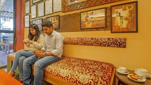 A couple sitting on a patterned sofa in a room with framed artwork on the walls. - Fabhotel 4 Pillar's - Nr Big Daddy Casino, Panaji (Panaji)