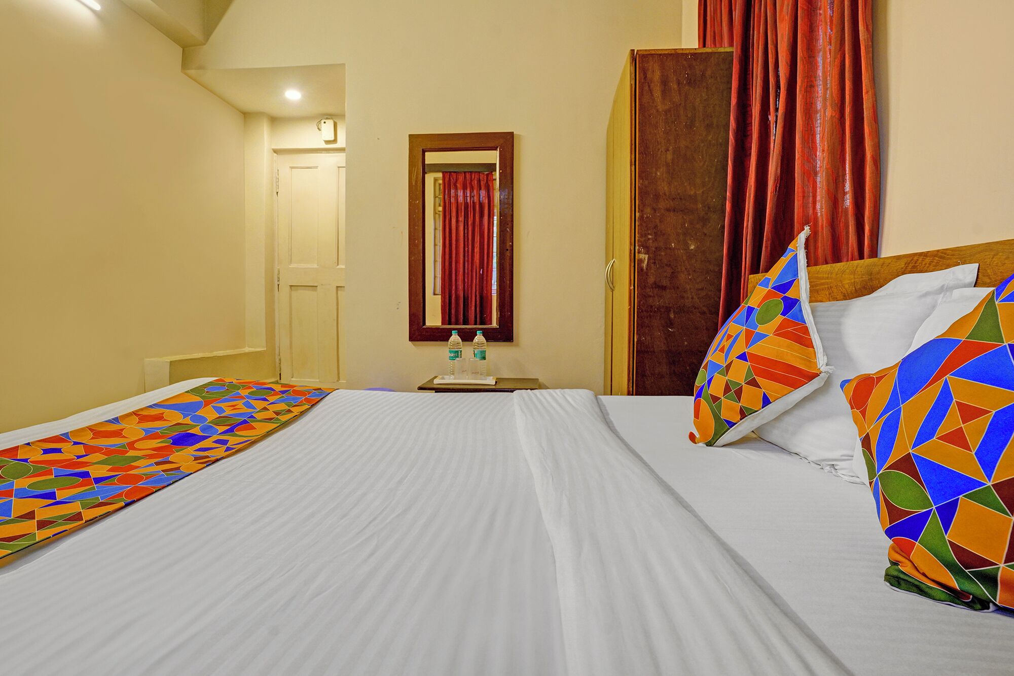 Una habitación de hotel con una cama grande, una mesita de noche con botellas de agua, un espejo y una puerta.