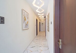 Un couloir doté d’un sol en marbre, des œuvres d’art encadrées accrochées aux murs et une porte en bois sur le côté droit.