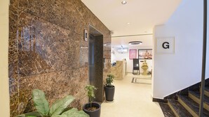 A hotel lobby with a marble wall, a reception desk, a Buddha statue, and a staircase. - Fabhotel Prime Atithyam (Gurugram)