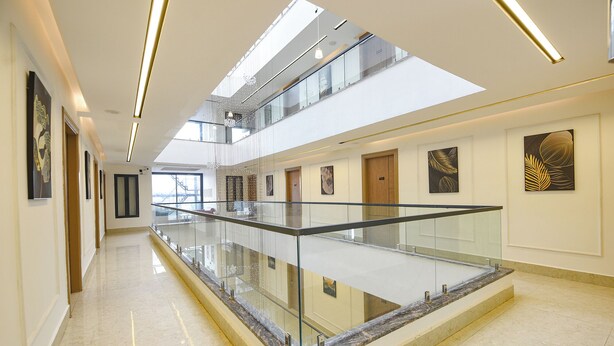 A modern hotel interior with a glass railing, multiple floors, and artwork on the walls. - Fabhotel Prime Atithyam (Gurugram)