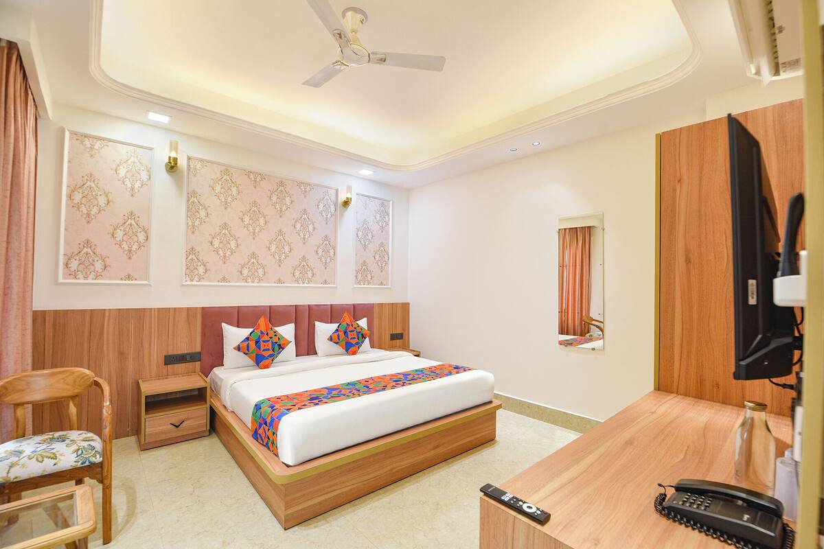A hotel room with a bed, wooden headboard, bedside tables, a desk with a telephone, and a ceiling fan.