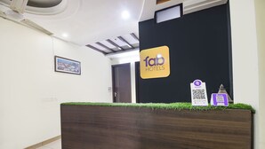 Un comptoir d’accueil avec une enseigne indiquant « fab hotels », un tableau encadré accroché au mur et deux codes QR posés sur le comptoir.
