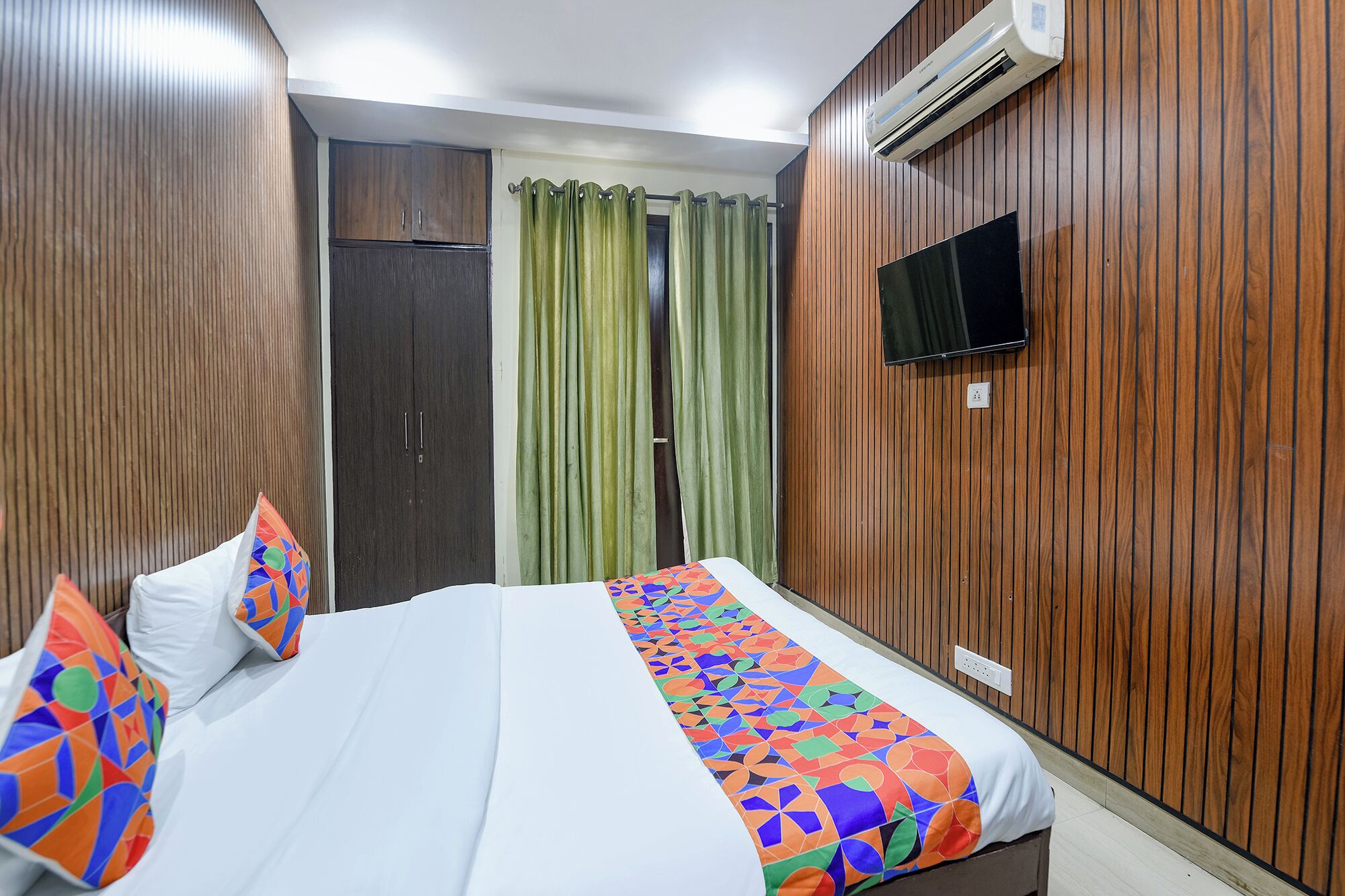 Habitación de hotel con cama, televisor en la pared y detalles en paneles de madera.