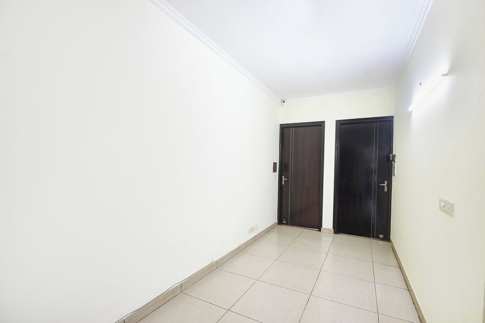A hallway with two dark wooden doors, white walls, and a tiled floor.