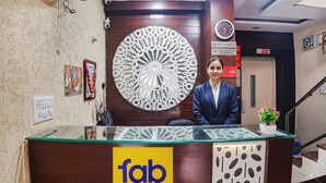 A reception desk with a glass top and a logo for 'fab hotels'. There is a decorative wall piece behind the desk and a clock on the wall. - Fabhotel Shri Vilas (Bhopal)