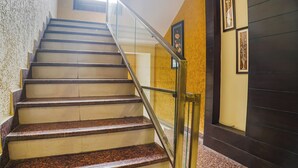 A staircase with a glass railing, leading to a room with a dark wooden door and framed artwork on the wall. - Fabhotel Shri Vilas (Bhopal)