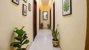 A hallway with framed artwork on the walls, potted plants, and a mirror at the end. - Fabhotel Shri Vilas (Bhopal)