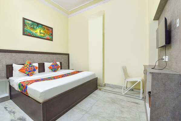 A hotel room with a bed, a desk, a chair, a TV, and a painting on the wall.