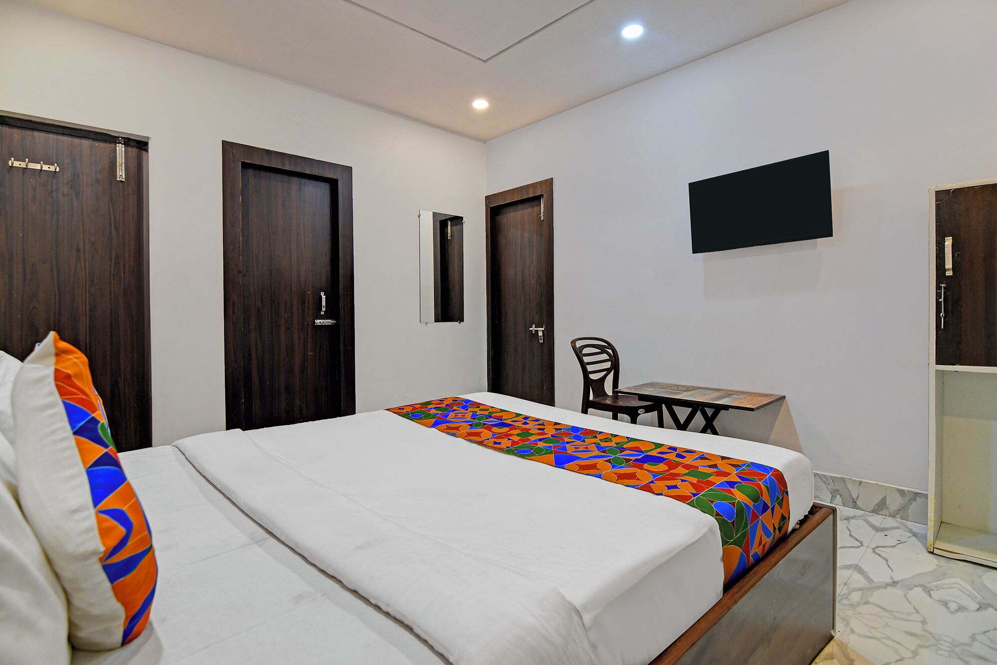 Une chambre d’hôtel avec un lit, une petite table, une chaise et un téléviseur fixé au mur.