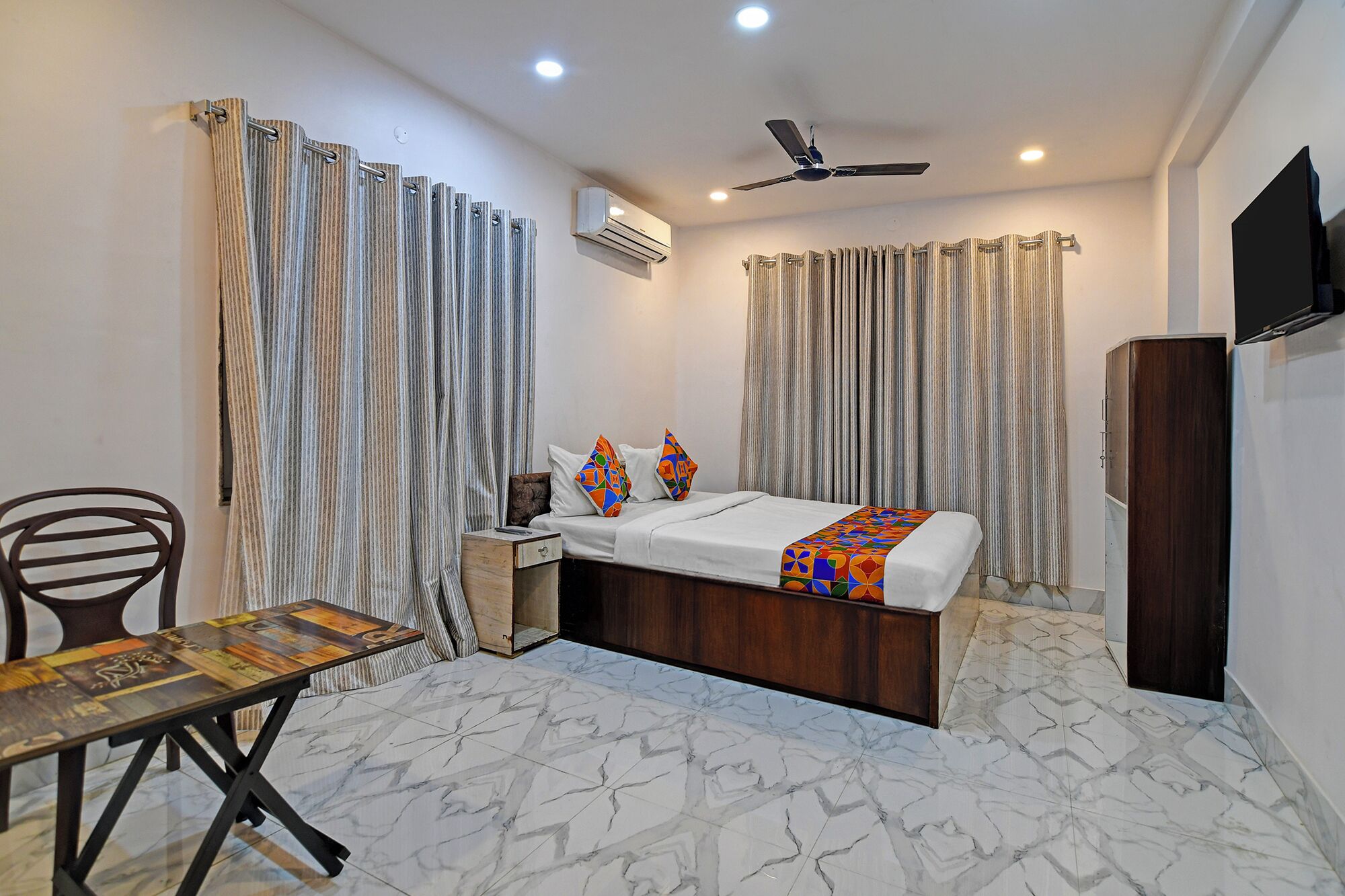 A bedroom with a bed, a desk, a chair, curtains, a ceiling fan, and an air conditioning unit.