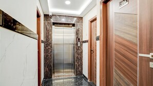 A hallway with a marble floor, a wooden door with a number plate, and an elevator. - Fabhotel Leon Square (Bengaluru)