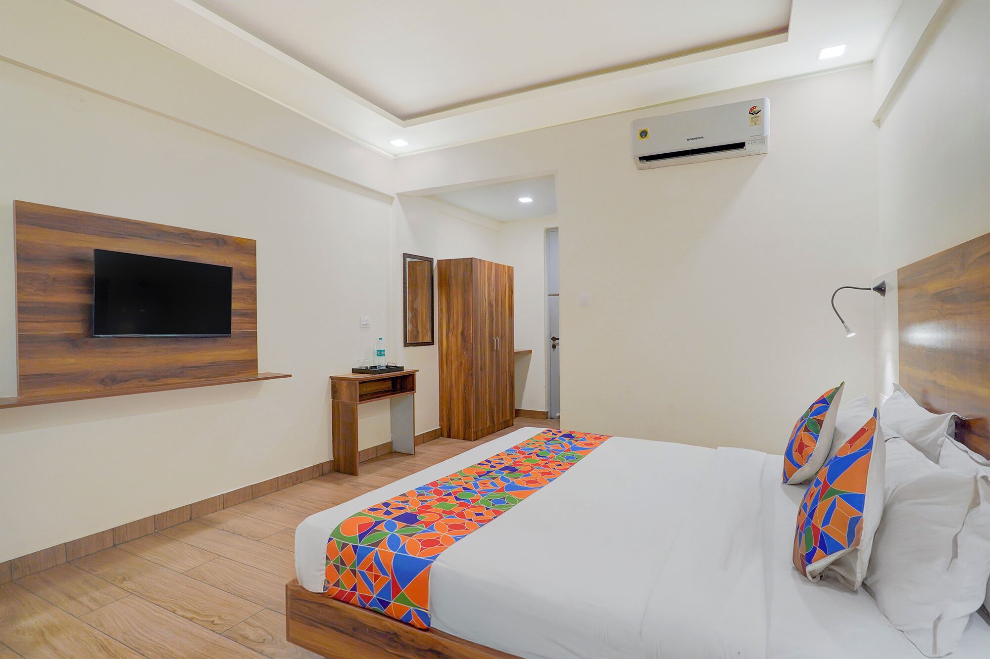 A modern hotel room with a bed, a TV mounted on the wall, a wardrobe, and a desk.