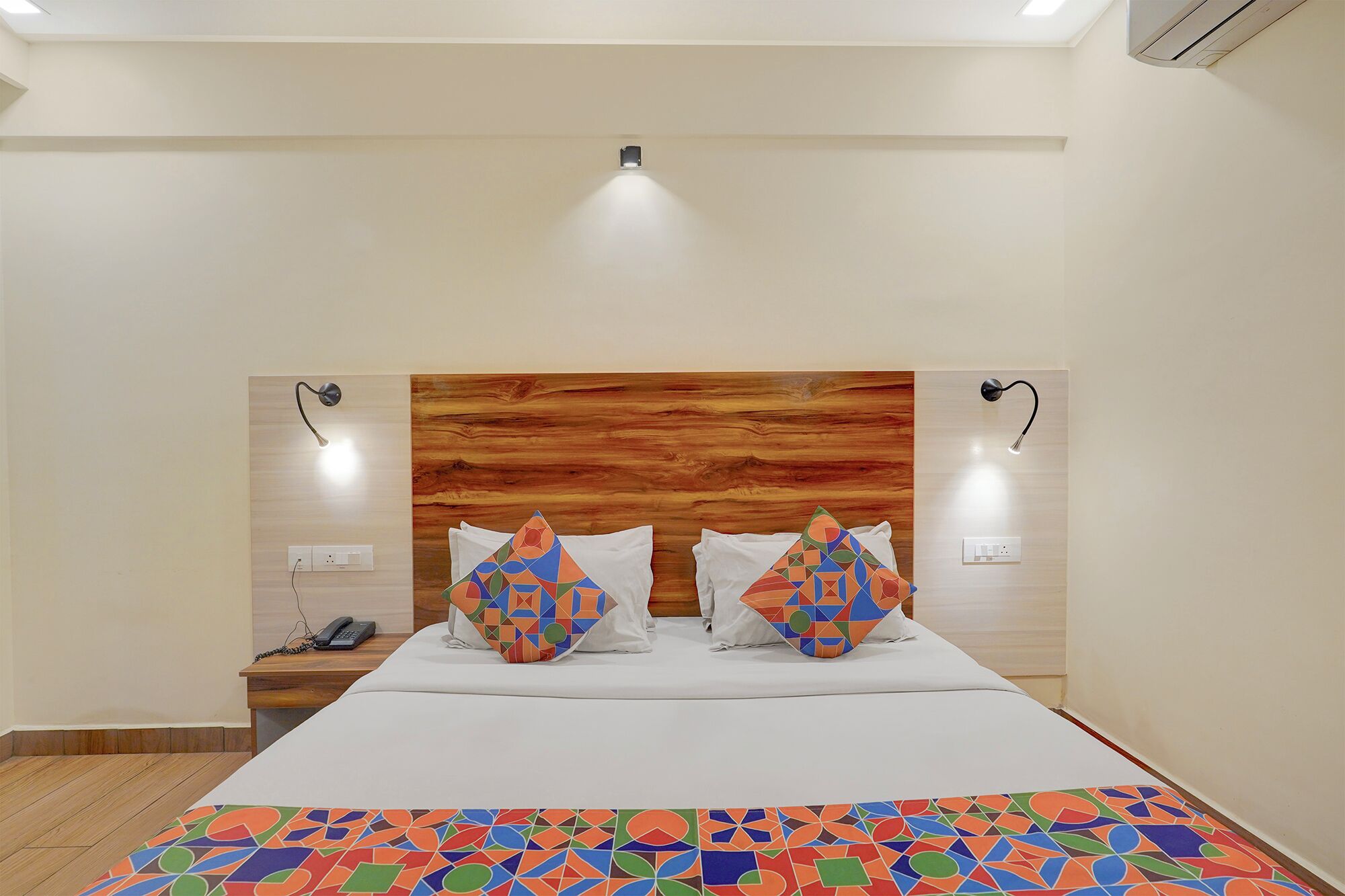 Camera d'albergo con una testiera in legno, due abat-jour, un telefono e una coperta colorata con motivo geometrico.