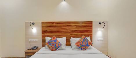 Camera d'albergo con una testiera in legno, due abat-jour, un telefono e una coperta colorata con motivo geometrico.
