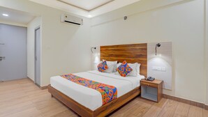 Una habitación de hotel moderna con cabecera de madera, cama con ropa de cama geométrica colorida, mesita de noche con lámpara y unidad de aire acondicionado en la pared.