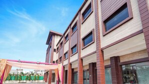 A multi-story building with a modern architectural design, featuring a mix of brick and plaster exteriors, large windows, and a covered entrance area. - Fabhotel Palm Bliss (Unnao)
