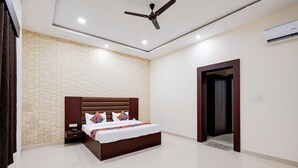 A modern hotel room with a large bed, a ceiling fan, and a tiled wall. - Fabhotel Palm Bliss (Unnao)