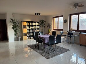 A spacious living area with a dining table, chairs, a bookshelf, and a kitchen area.