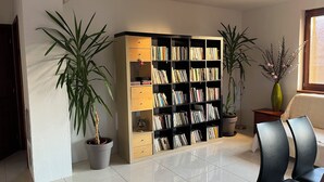 Un salon avec une bibliothèque, deux plantes en pot et un fauteuil.