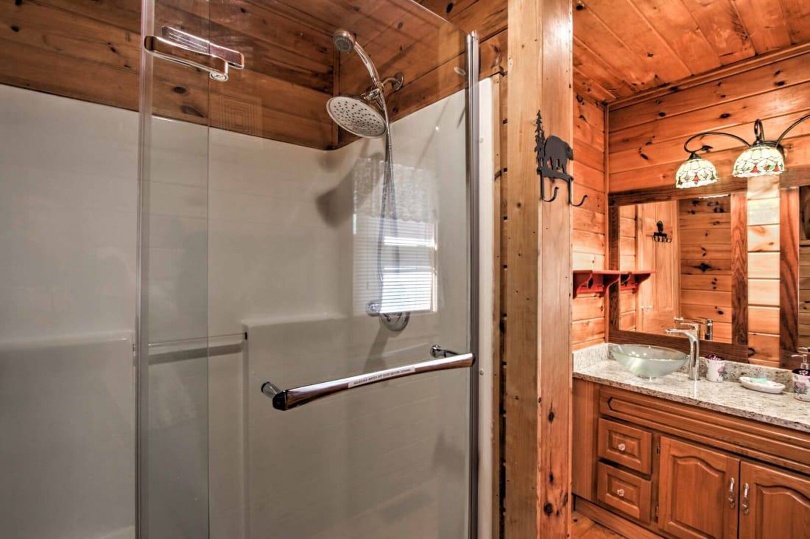 A wooden cabin bathroom with a glass shower enclosure, a sink with a mirror, and wooden cabinets.