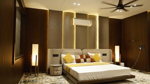 A modern bedroom with a large bed, bedside lamps, an air conditioning unit, and a ceiling fan. - Siya Residency (New Delhi)