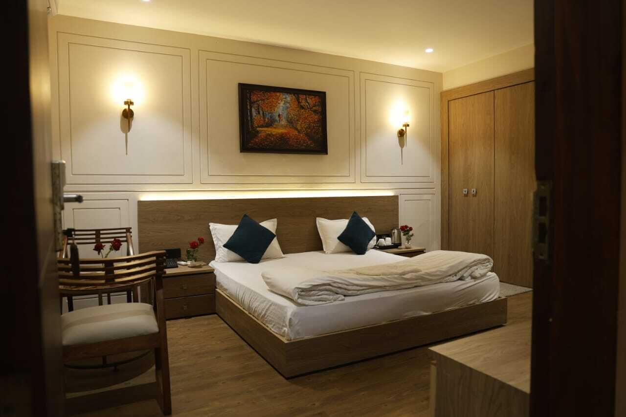 A bedroom with a large bed, two wall-mounted light fixtures, a painting, and a wooden wardrobe.