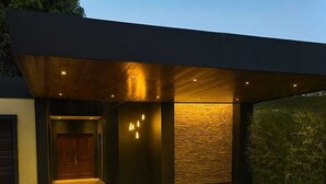 Un edificio moderno con un acceso cubierto, un muro de piedra y un patio con baldosas verdes.