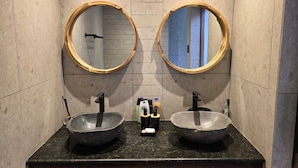 Un baño con dos espejos redondos, encimera de granito y dos lavamanos.