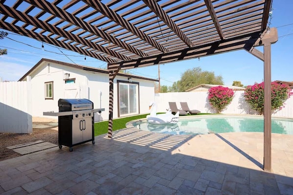 Un espace extérieur abrité, doté d’un barbecue, d’une piscine et d’un bâtiment blanc.