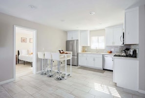 Une cuisine moderne avec des meubles blancs, un réfrigérateur en acier inoxydable et un coin repas avec des chaises blanches.