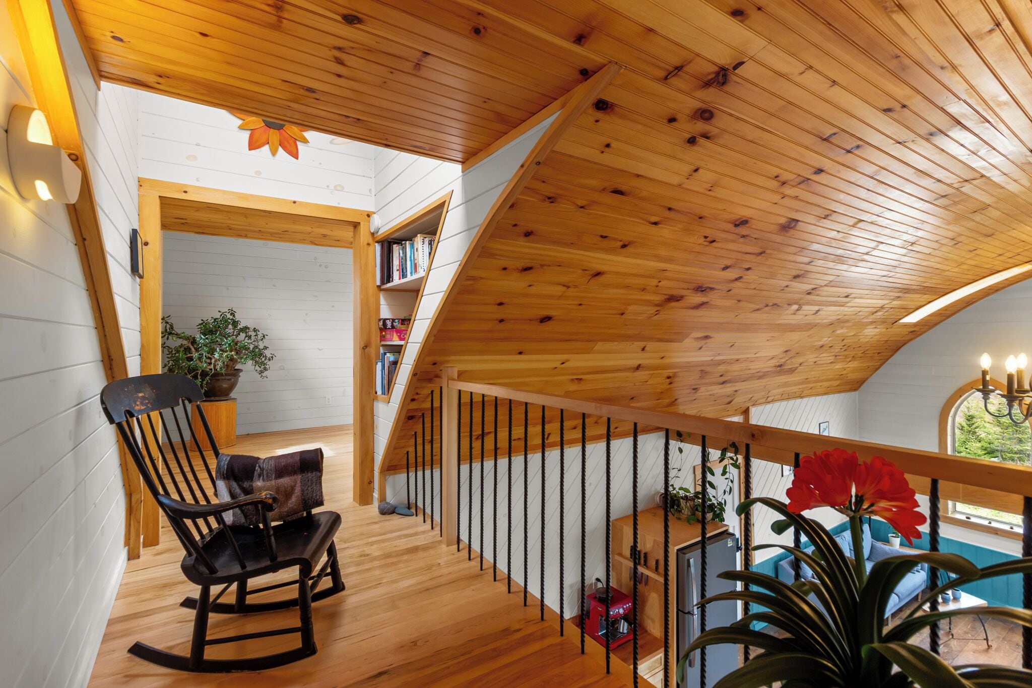 A wooden interior with a sloped ceiling, a rocking chair, a bookshelf, and a view of the outdoors.