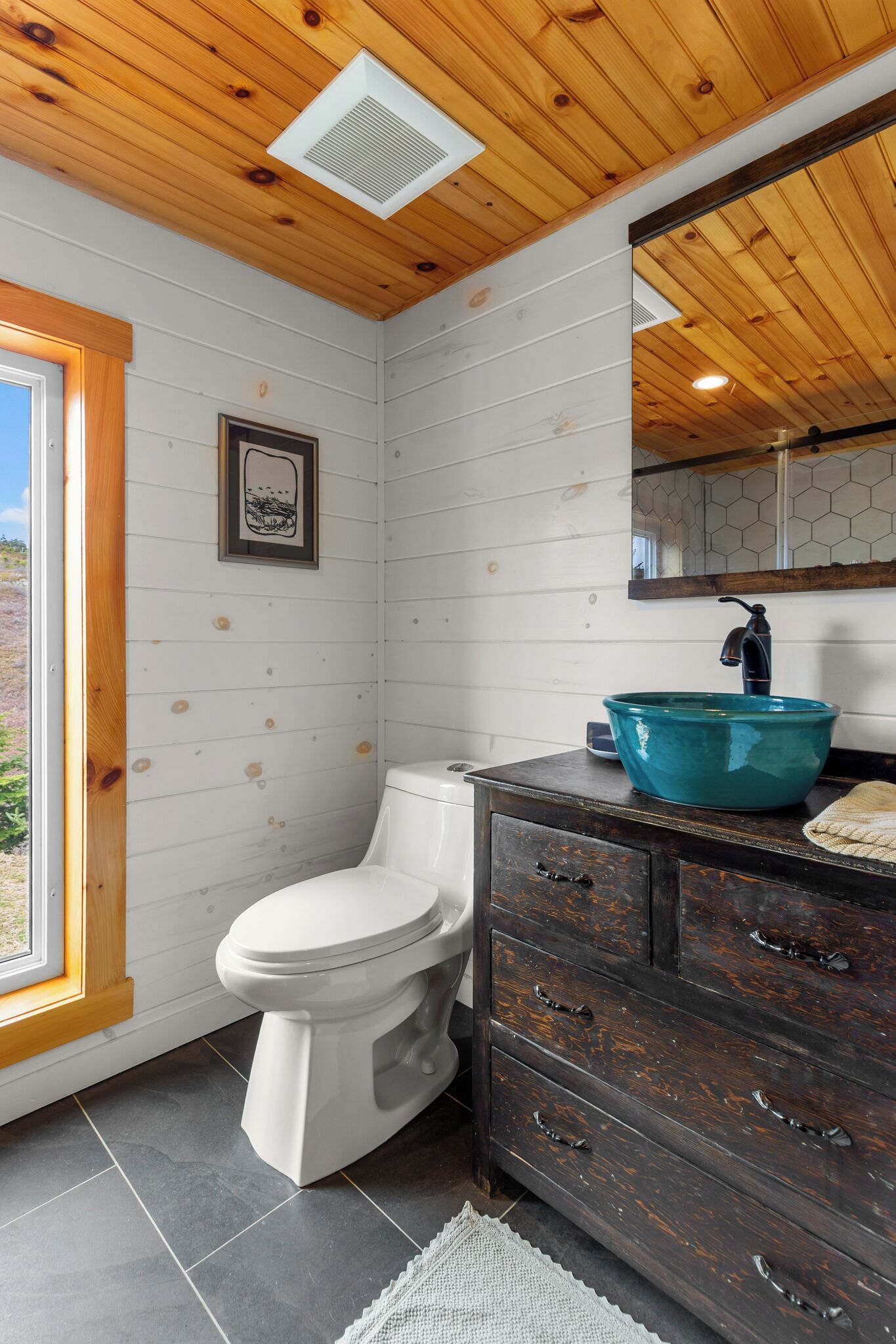 A bathroom with a white toilet, a dark wooden vanity with a teal sink, and a large mirror above the vanity.