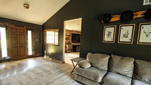 A living room with a sofa, wooden flooring, and a kitchen in the background.