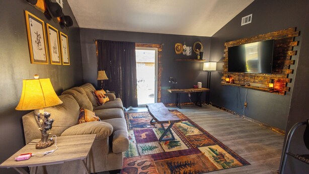 A living room with a sofa, a coffee table, a TV mounted on a wooden wall, and a patterned rug.