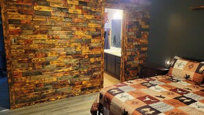 A bedroom with a wooden wall, a bed with patterned bedding, and a nightstand.