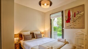 A well-lit bedroom with a large bed, bedside lamps, a window with a view, and a painting on the wall. - Deauville Lovely Flat With Private Garden (Tourgeville)