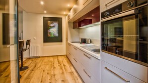 A modern kitchen with wooden flooring, white cabinets, and a built-in oven. - Deauville Lovely Flat With Private Garden (Tourgeville)