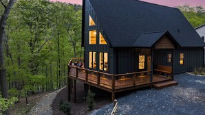 Una cabaña oscura con terraza, rodeada de árboles.