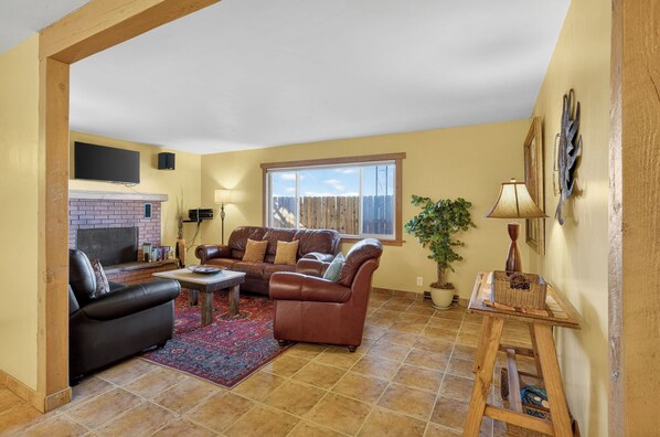 A living room with a fireplace, leather sofas, a coffee table, and a large window.