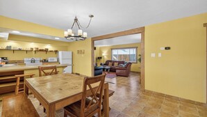 Un amplio salón con una mesa de comedor de madera, un sofá y una cocina con refrigerador y estanterías.